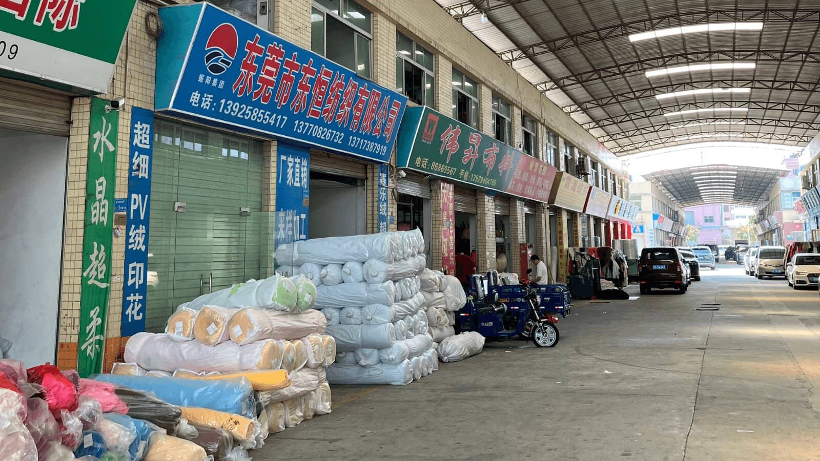 東莞の生地・副資材市場。店舗の前に生地のロールが山積みになっている